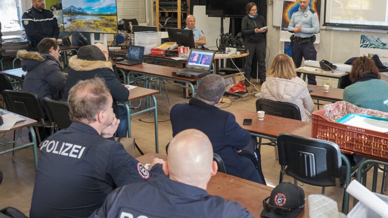 Agrandir l'image Dans une pièce ressemblant à une salle de classe, des plongeurs de la gendarmerie nationale, des plongeurs Suisse et Allemand, écoutent attentivement le directeur des opérations qui présente l'exercice qui va se dérouler.