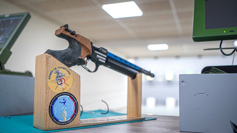 Agrandir l'image Photo de l'arme de tir posée sur un socle en bois. sur celui-ci on peut voir deux rondaches dont un de l'armée des champions, et l'autre des sportifs de haut niveau de la défense.