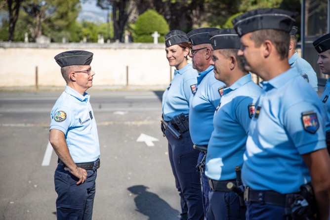 Le major g&eacute;n&eacute;ral de la gendarmerie nationale se tient debout, souriant, maisn sur les hanches, face &agrave; quatre gendarmes align&eacute;s c&ocirc;te &agrave; c&ocirc;te.