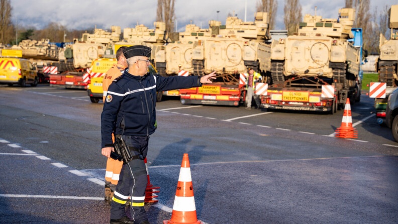 Un gendarme devant le convoi à l'arret, en train de montrer quelques choses du doigt.