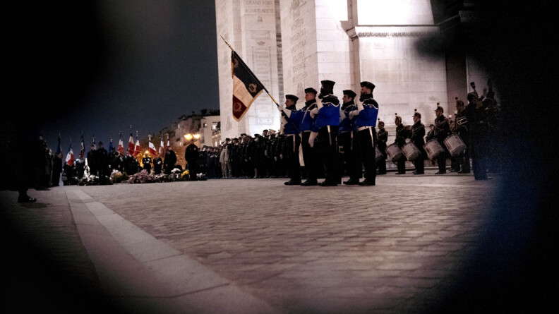 Un gendarme, entouré de quatre camarades, porte le drapeau français devant l'Arc de Triomphe, lors de la cérémonie de clôture des JNR, le 12 novembre, à Paris. Il fait nuit.