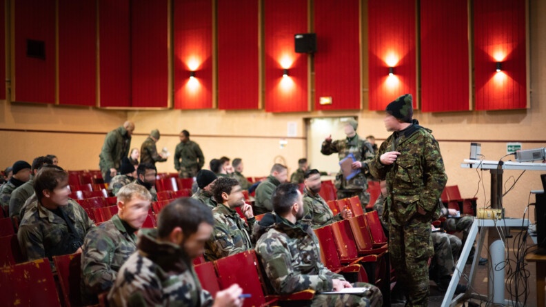 Les stagiaires sont dans un amphithéâtre rouge où ils écoutent un formateur.