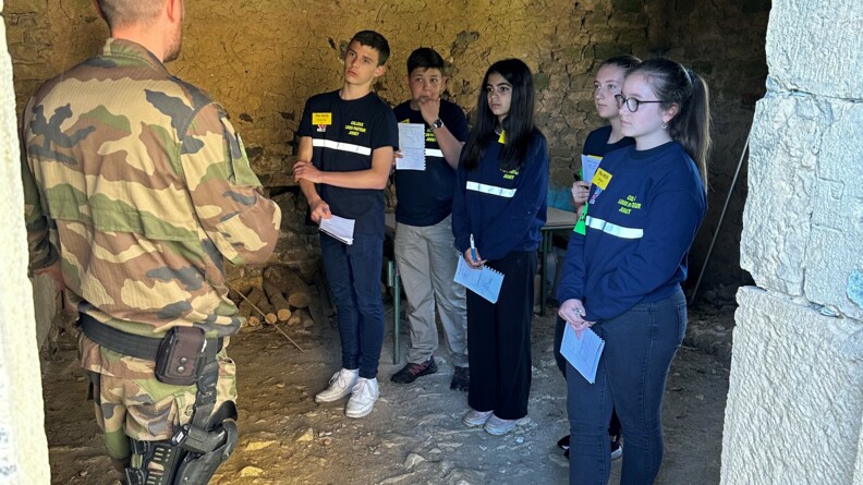 A l'intérieur d'une grange sur le sol en terre battue, cinq élèves, carnet à la main, écoutent attentivement un gendarme en treillis.