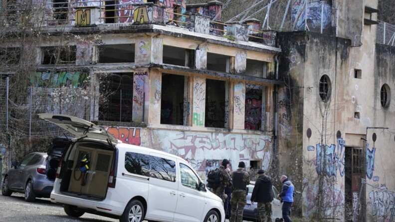 des gendarmes en bleu et un treillis devant des bâtiments tagués et anciennement brûlés
