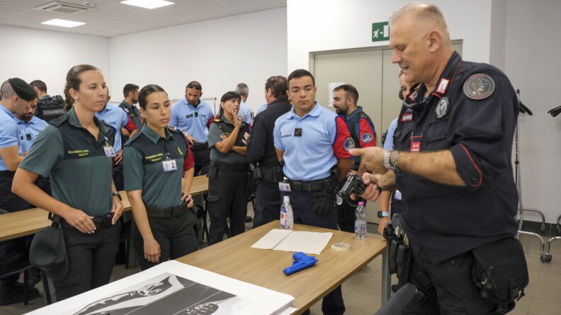 Un cadre italien montre comment fonctionne le pistole Beretta à des stagiaires. Sur la table est posé un blue gun, un chargeur et une cible.