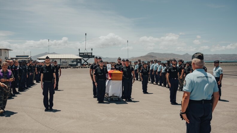 Un cercueil de gendarmes sur un tarmac porté et entouré par ses camarades au garde-à-vous