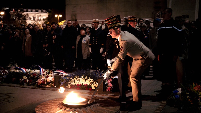 Un militaire est pench&eacute; vers la Flamme de la nation, &agrave; l'Arc de Triomphe, s'appr&ecirc;tant &agrave; la raviver