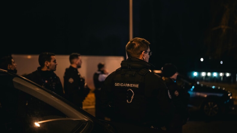Vue de dos de plusieurs gendarmes qui regardent vers la droite de l'image. Il fait nuit et sombre.