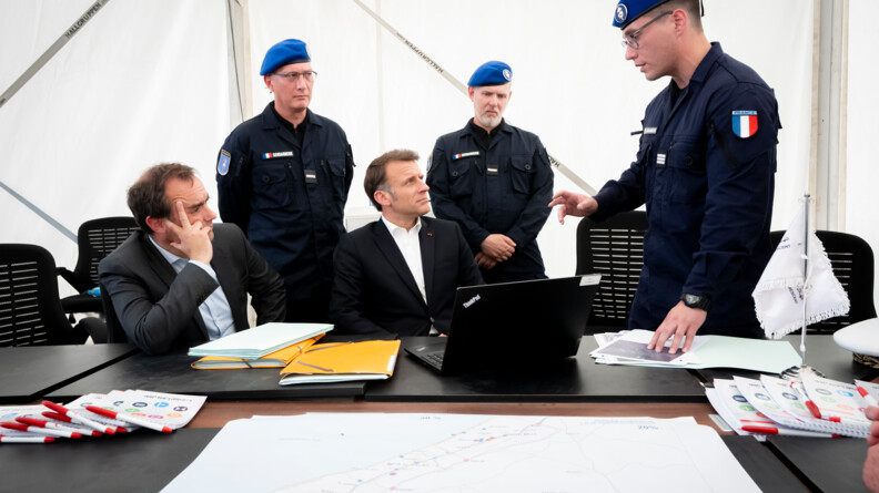 Agrandir l'image Le président de la République, assis, en train d'écouter un gendarme, portant un bérêt bleu, debout, de profil. En arrière plan deux autres gendarmes dans la même tenue.