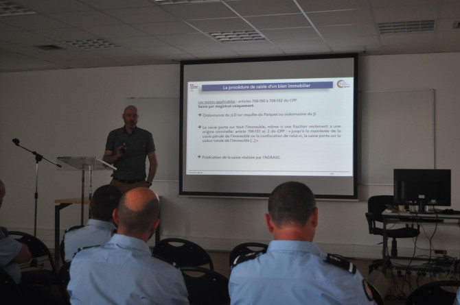 La photo repr&eacute;sente un homme, debout, face &agrave; une assembl&eacute;e de gendarmes, s'exprimant au micro. Derri&egrave;re lui ets projet&eacute;e une pr&eacute;sentation power point.