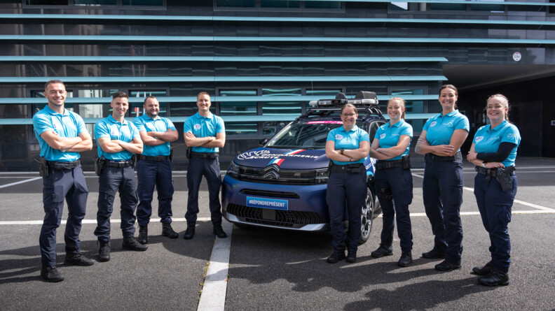 De part et d'autre d'un véhicule gendarmerie du Tour de France, 4 hommes et 4 femmes de la gendarmerie, bras croisés
