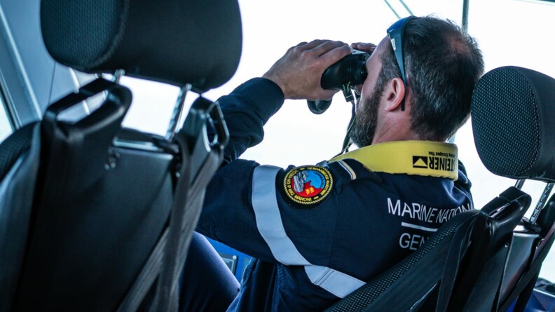 Un gendarme de la maritime dans un bateau, regarde dans des jumelles.
