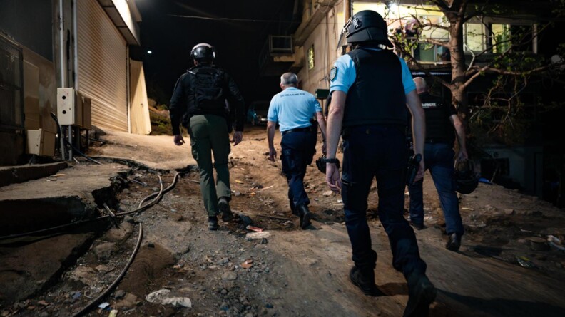 Le directeur g&eacute;n&eacute;ral de la gendarmerie de dos, entour&eacute; par trois autres gendarmes. Ils sont entrain de gravir une pente d&eacute;vaster. Il fait nuit.
