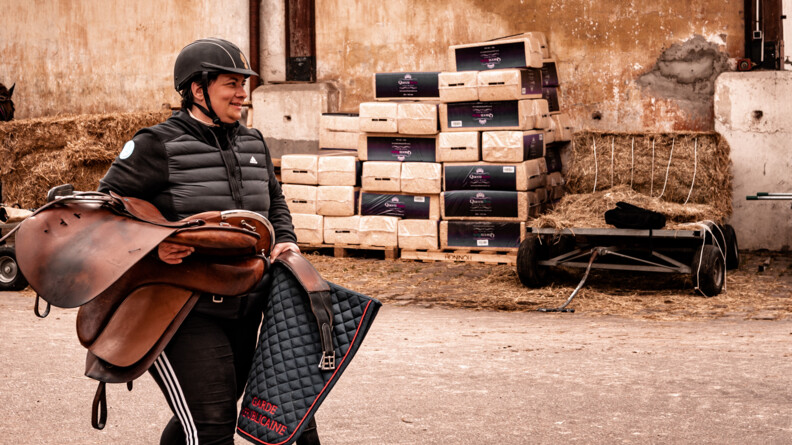 Laetitia, participante au stage Cent'Or, marche en portant la selle de son cheval et le tapis marqué Garde républicaine.