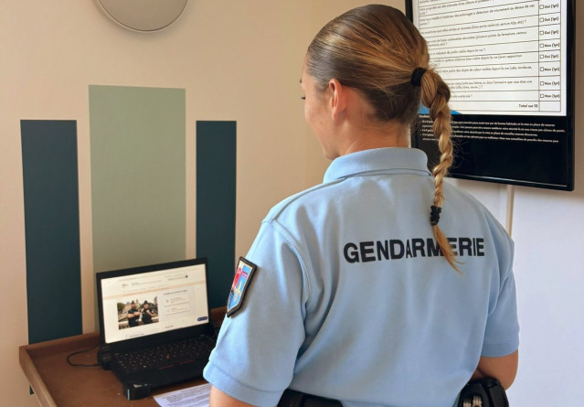 Une gendarme, de dos, devant un ordinateur portable ouvert sur une table.