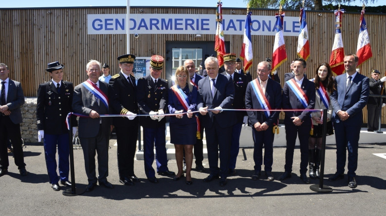 Le ministre délégué au ministère de l'Intérieur, entouré d'autorités et d'officiels, coupant un ruban tricolore devant la façade d'une brigade de gendarmerie