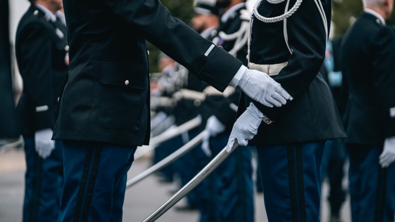 Agrandir l'image deux gendarmes face à face en tenue de cérémonie, l'un a le foureau relevé, l'autre touche son galon de manche