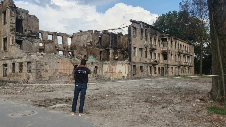 Un expert de l'IRCGN vu de dos, en train de photographier les d&eacute;combres d'un b&acirc;timent.
