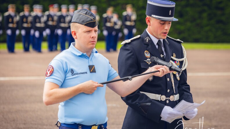 Agrandir l'image un élève-gendarme lit un texte tandis que d'un autre élève, en tenue d'intervention, lui tend le micro
