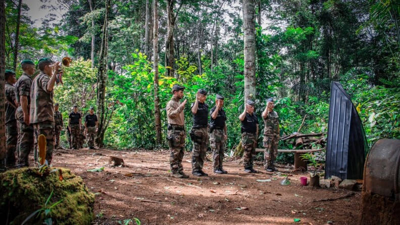Agrandir l'image Le DGGN, le CGOM et le COMGEND, en polo noir et pantalon de treillis, entourés de deux militaires en treillis kaki, au garde-à-vous, devant une stèle en forme de pointe de pirogue, érigée au milieu de la forêt amazonienne.