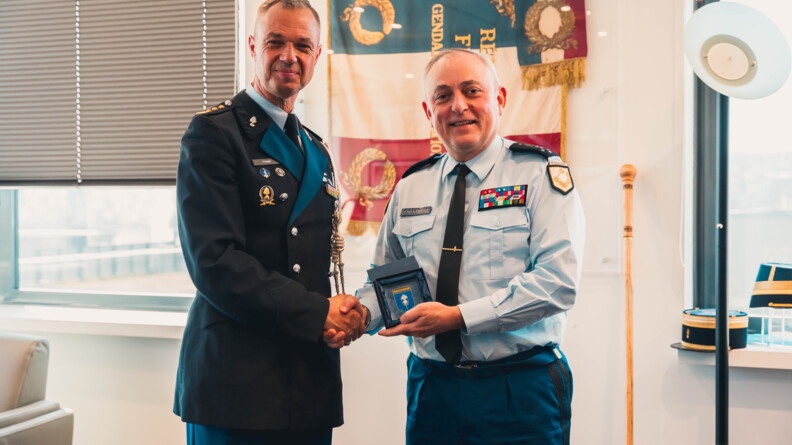Deux militaires (le DGGN et le commandant de la FGE) se serrent la main, souriants, en regardant l'objectif. L'un d'eux tient une médaille dans sa main.