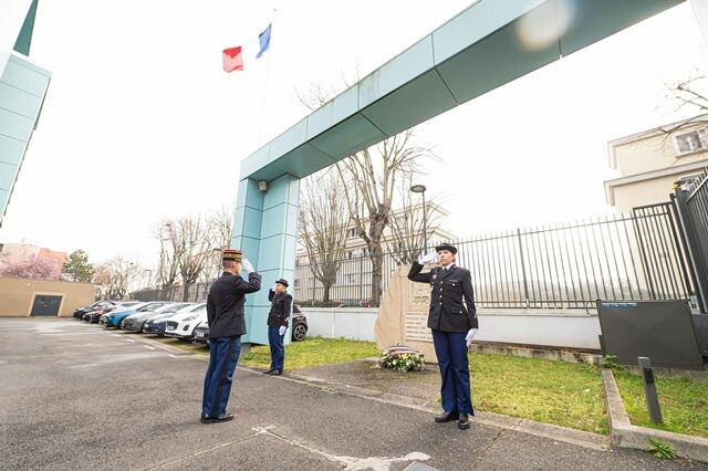 Le major g&eacute;n&eacute;ral de la gendarmerie, vu de trois-quart dos, saluant devant la st&egrave;le de la gendarmerie, au pied de laquelle a &eacute;t&eacute; d&eacute;pos&eacute;e une gerbe de fleurs, avec deux gendarmes au salut de part et d'autre.
