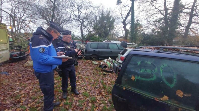 Deux gendarmes relevant les éléments au milieu d'un champ de véhicules épaves