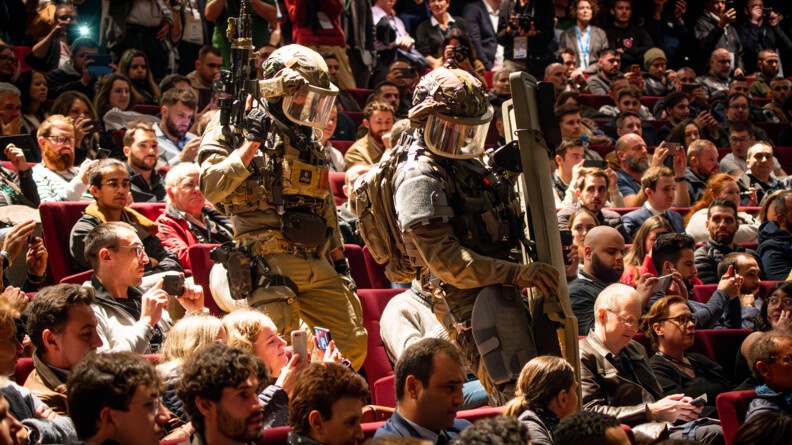 Deux hommes du GIGN descendent au sei nd'un amphith&eacute;&acirc;tre plein, les gens les filment et prennent des photos