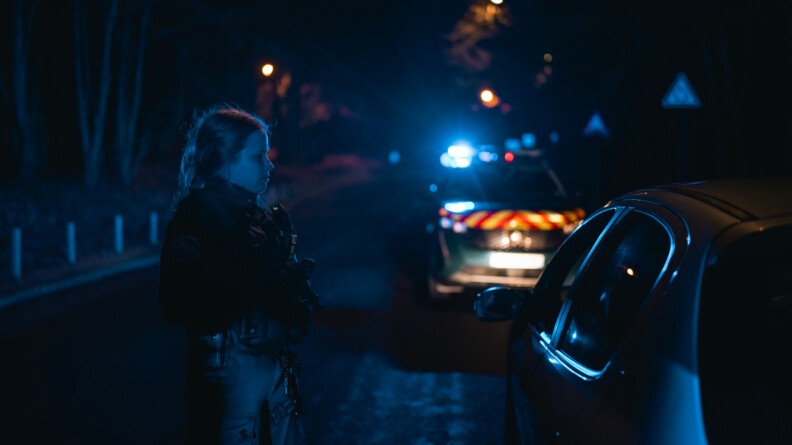 Une gendarme devant une voiture. Il fait nuit et sombre.
