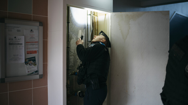 Agrandir l'image Un gendarme inspecte les parties communes d'un immeuble avec une lampe torche.