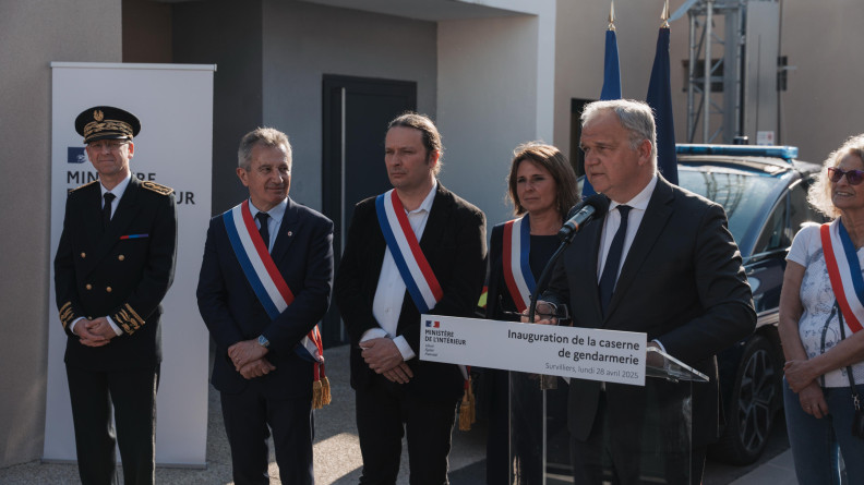 Un préfet et quatre élus, et un homme en complet noir derrière un pupitre transparent portant la mention "inauguration de la caserne de gendarmerie"