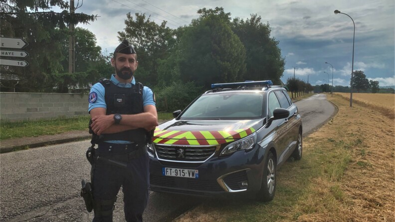 Un gendarme est devant une voiture gendarmerie. Il prend la pose pour la photo.