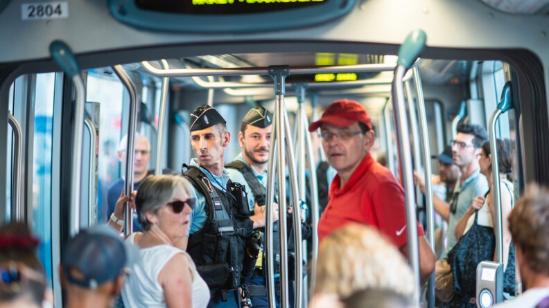 Photo prise dans une rame de tramway : au premier plan et sur les côtés, des passagers, et au milieu de la photo, deux gendarmes de profil.