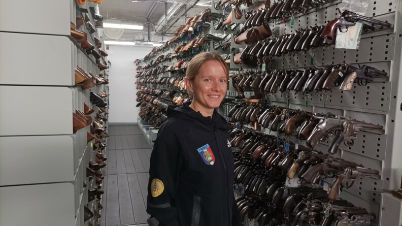 La para-sportive Gaëlle Edon, Sportive de haut-niveau de la Défense - Gendarmerie (SHND-G), devant des rangées d'armes à feu, à l'Institut de recherche criminelle de la gendarmerie nationale.