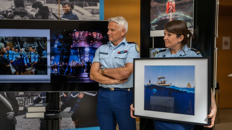La gendarme tient dans ses mains la photo du major Mathieu Rochault qui a &eacute;t&eacute; choisi par Martin Bureau. Derri&egrave;re elle, se tient le g&eacute;n&eacute;ral Lettermann. La photo est prise dans l'eau, &agrave; moiti&eacute; submerg&eacute;e. On peut apercevoir des plongeurs et le bateau.
