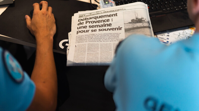 Agrandir l'image Photo montrant deux gendarmes de dos devant un journal titrant "Débarquement de Provence : une semaine pour se souvenir"