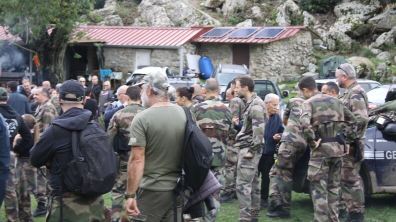 Agrandir l'image De nombreux militaires sont rassemblés sur une pelouse, à proximité d'une bergerie corse. On aperçoit un véhicule de la gendarmerie. Quelques civils se mêlent au groupe.