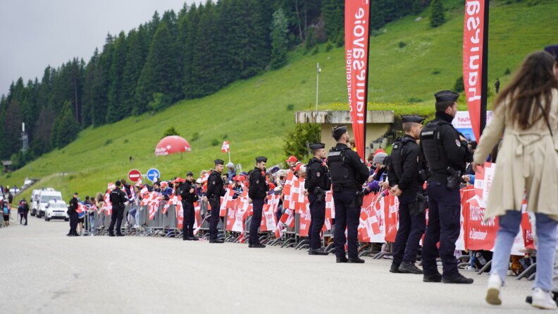 Le long d'une route au pied de la montagne, une dizaine de gendarmes mobiles sont en sécurisation tandis que la population, munie de drapeaux de la haute-savoie, patiente derrière des barrières