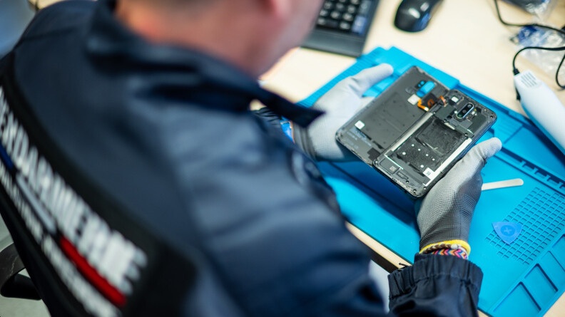 Un gendarme de dos entrain d'ouvrir un t&eacute;l&eacute;phone pour y d&eacute;couvrir son contenu num&eacute;rique.