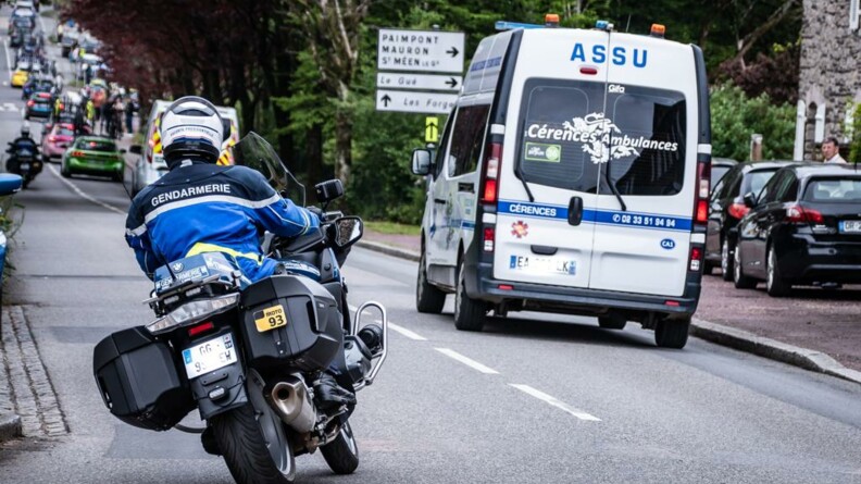 Un motocycliste d'EDSR vu de dos, assurant l'escorte de la fin de course où se trouve un véhicule de secours.