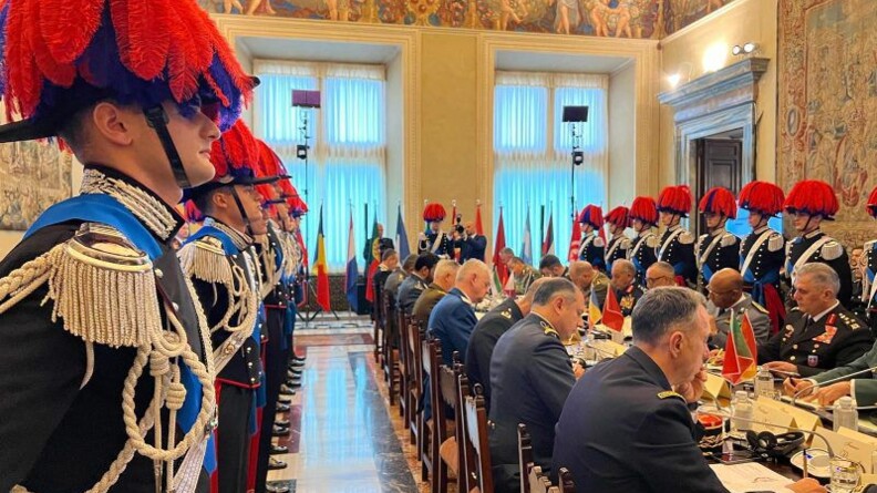 Des membres des forces de gendarmerie et de police &agrave; statut militaire sont r&eacute;unis autour d'une grande table lors d'une s&eacute;ance de travail. Ils sont entour&eacute;s par des Gardes de l&rsquo;Arme des carabiniers posant debout, en tenue, tout autour de la table.