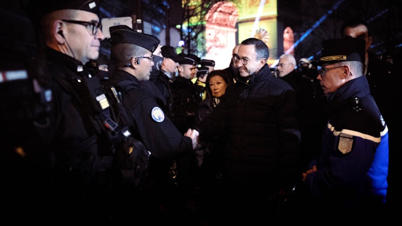 Dans la nuit, le ministre de l'Intérieur salue un gendarme mobile. Le major général de la gendarmerie se trouve à sa droite.