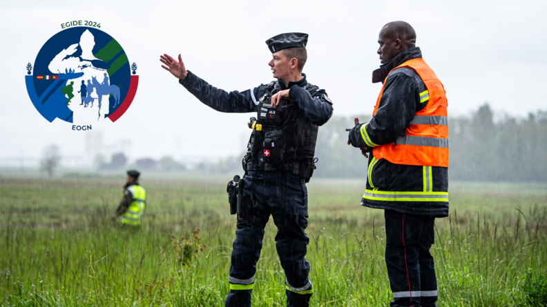 Agrandir l'image Un élève officier montre une direction à un officier pompier lors d'une intervention sous le pluie, d'un accident de bus avec une personne disparue