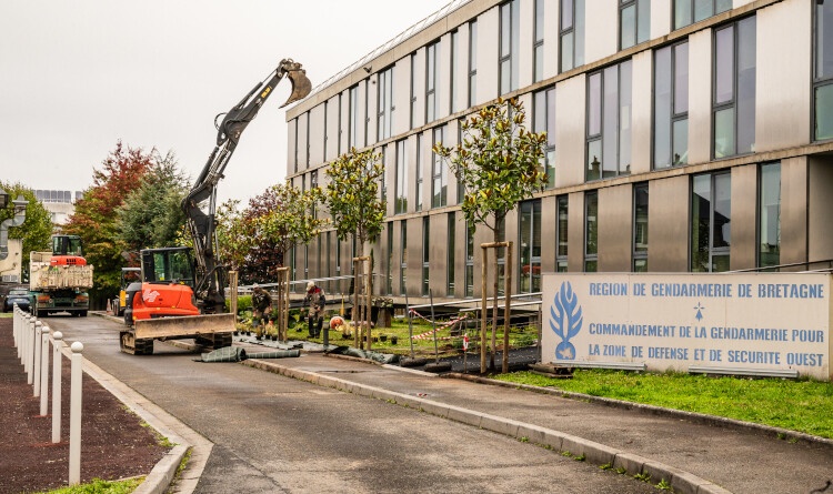 Image d'un grand b&acirc;timent gris, devant lequel est appos&eacute;e une grande pancarte portant l'inscription en lettres bleues sur fond blanc "R&eacute;gion de gendarmerie de Bretagne". Des engins de travaux manoeuvrent dans l'all&eacute;e deva,nt le b&acirc;timent.