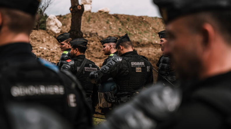 Un groupe de 5 gendarmes mobiles devant un talus de terre. En flou au premier plan, deux autres gendarmes mobiles qu'on devine