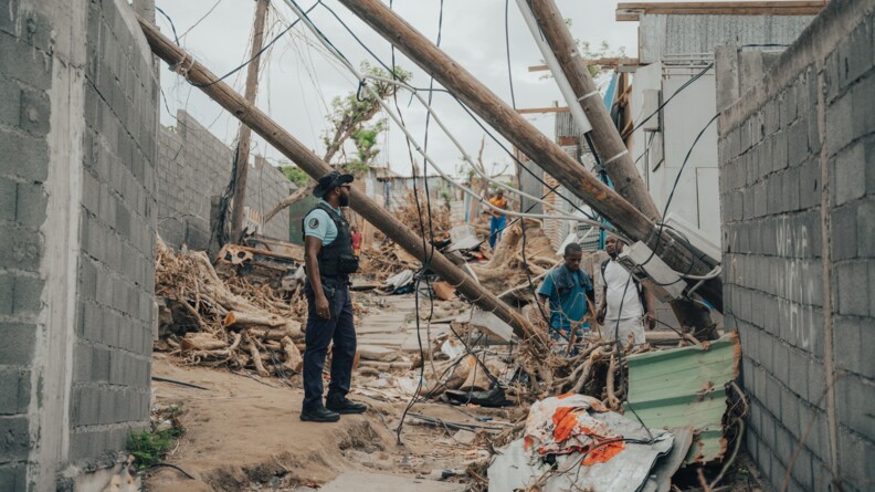 Un gendarme au milieu des ruines d'habitations. A c&ocirc;t&eacute; de lui se trouve quelques habitants.