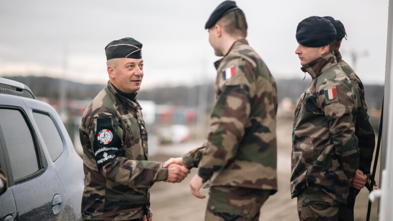 Agrandir l'image Un prévôt de trois quart droit, à gauche de l'image, serre la main d'un militaire de profil, qui a deux camarades de profil derrière lui