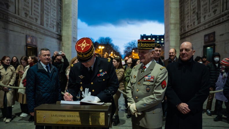 Un g&eacute;n&eacute;ral de gendarmerie en train de signer le livre de la flamme. A ses c&ocirc;t&eacute;s, un g&eacute;n&eacute;ral de l'arm&eacute;e de Terre et deux homme en civil.