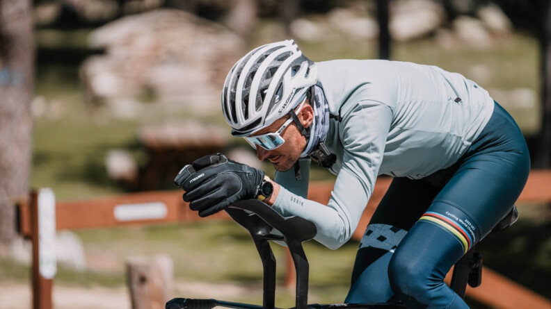 Un cycliste avance sur son v&eacute;lo, le corps pench&eacute; en avant. V&ecirc;tu d'une tenue bleue, il porte un casque, des lunettes de soleil blanches et des gants noirs.