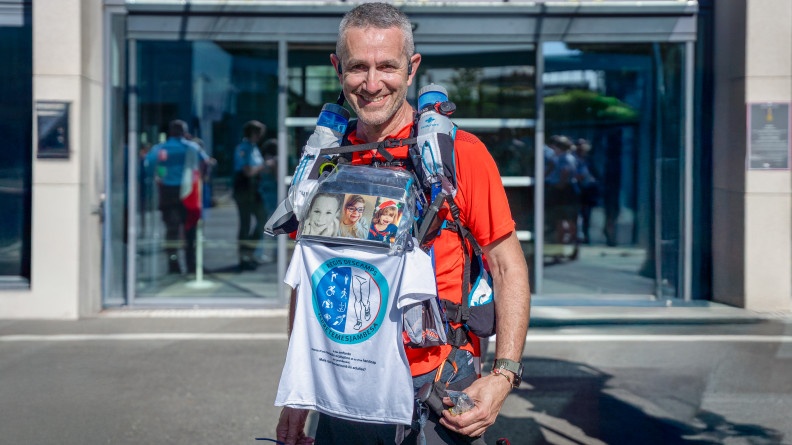 Un homme souriant en tenue de sport, porteur de photos d'enfant et d'un t-shirt blanc au logo bleu